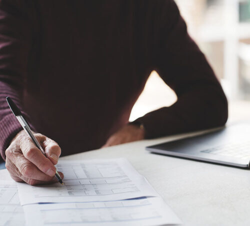 Hands, laptop and finance with a business man writing on documents at a desk in his office at work. Accounting, computer and contract with a male employee signing a document in the workplace